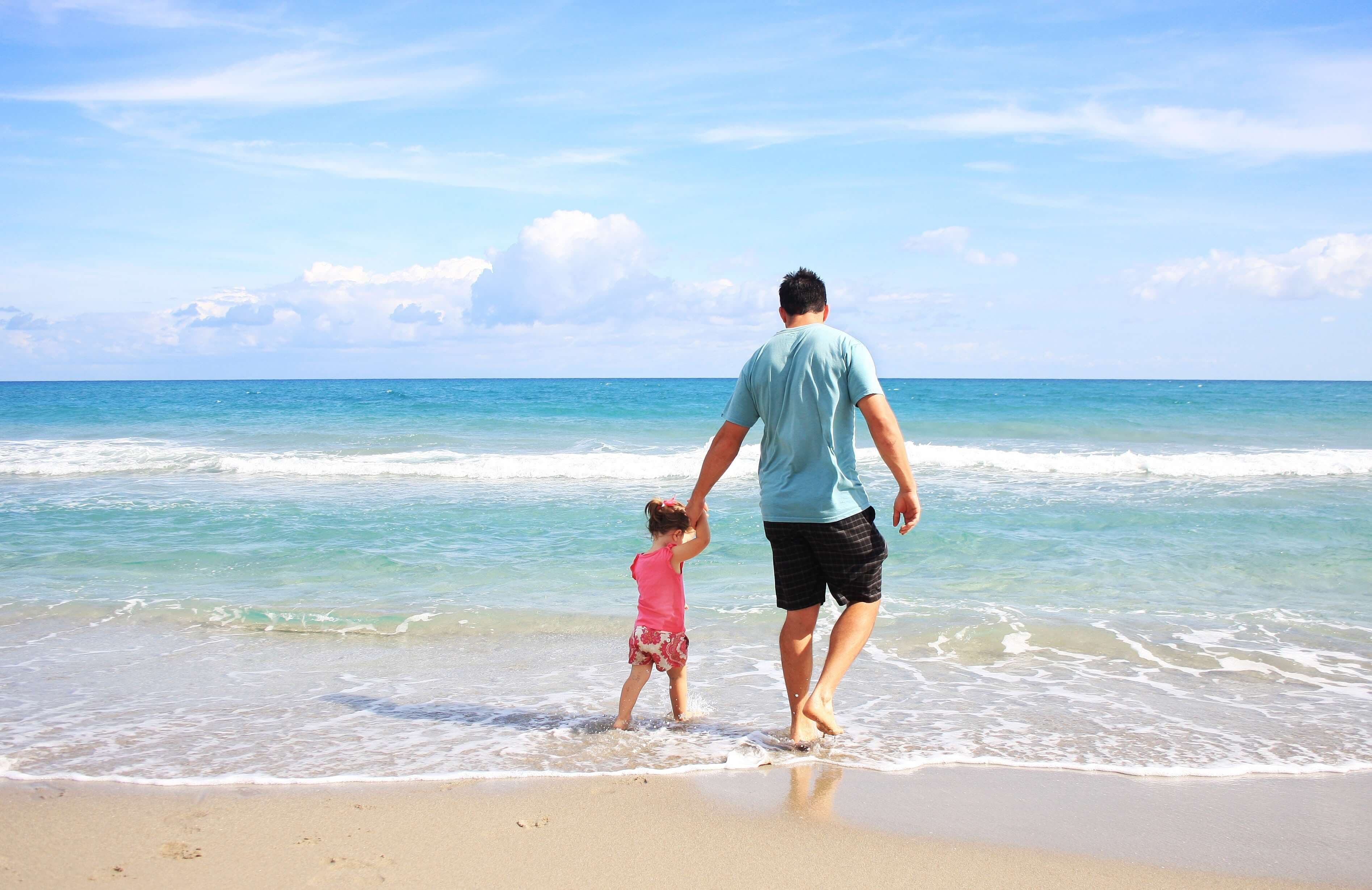 A father and young daughter walk along a beach